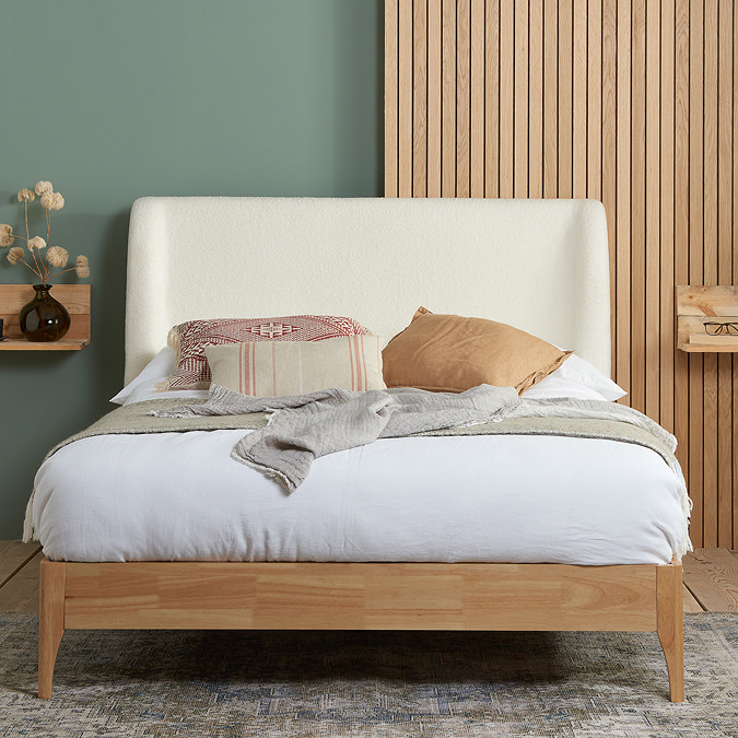 front on image of large wooden bed with white boucle headboard, dressed with mattress, sheets and cushions