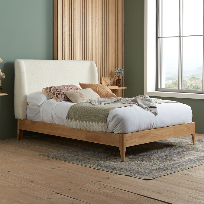 side on angled image of large double wooden bedframe with white boucle headboard and mattress dressed up on top.