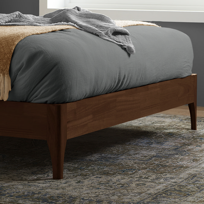 close up on foot of the bed where slim walnut brown legs rest on patterned rug of a bedroom
