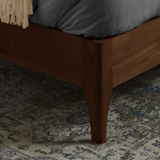 close up on walnut brown legs of evelyn bed on patterned rug