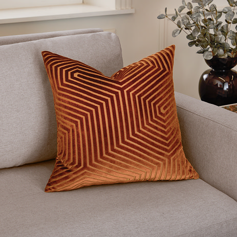 45x45cm brick coloured cushion with geometric detailing, sat in corner of cream sofa
