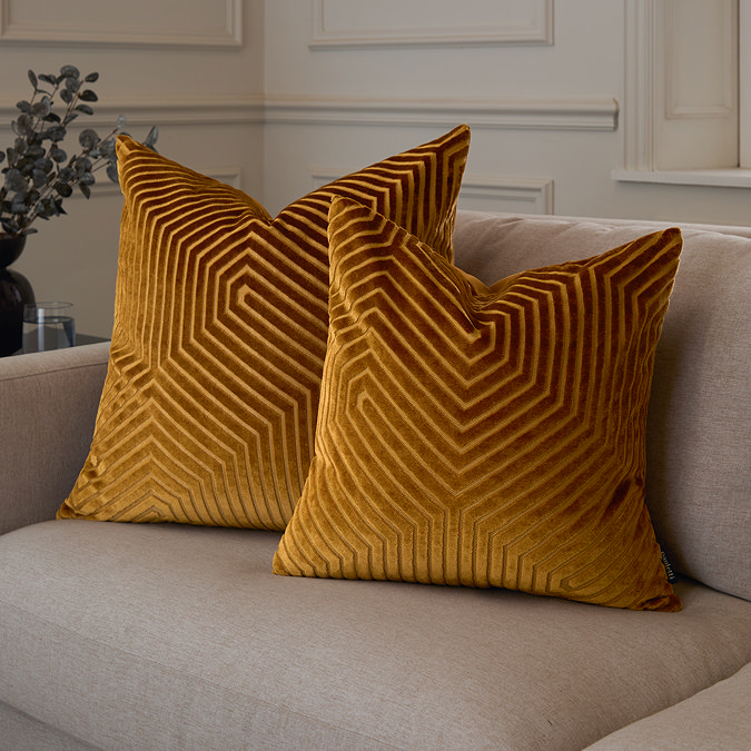 two sizes of gold velvet square cushion, 45x45 and 55x55cm, sat together on a cream sofa.