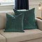 two sizes of teal green cut velvet geometric cushion, 45x45 and 55x55cm, sat together on a cream sofa.
