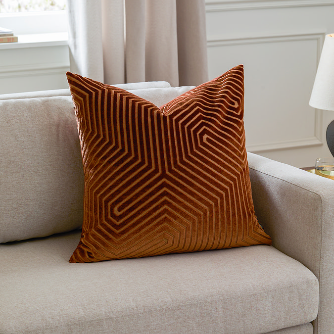 square brick coloured cushion with geometric detailing sat in the corner of a cream sofa