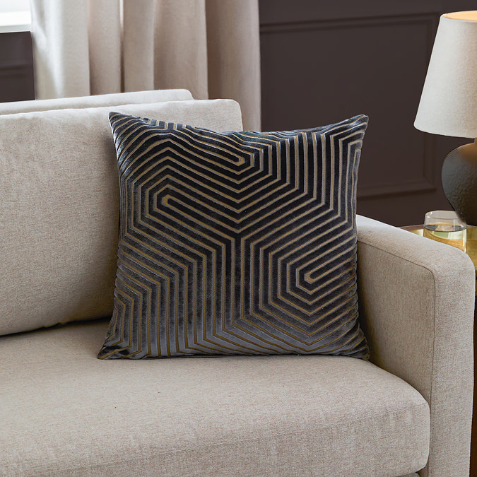 charcoal grey cushion with geometric detailing, sat in corner of cream sofa