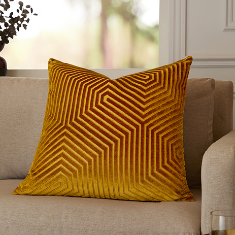 gold square cushion with geometric detailing, sat in corner of cream sofa