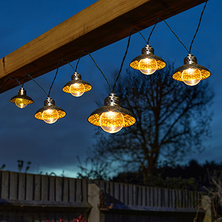 image of warm orange solar lights with semicircular tops and round bulbs, hung up at night in a garden