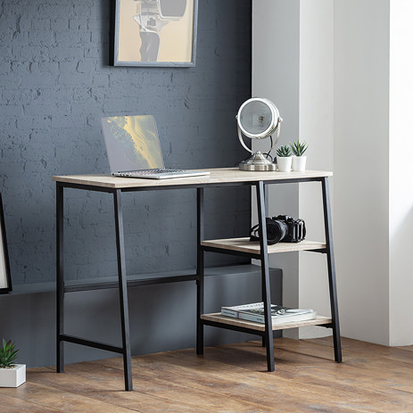 image of modern desk with sonoma oak top and black steel frame, with two open shelves to the right hand side, topped with a laptop, small lamp and two small faux plants