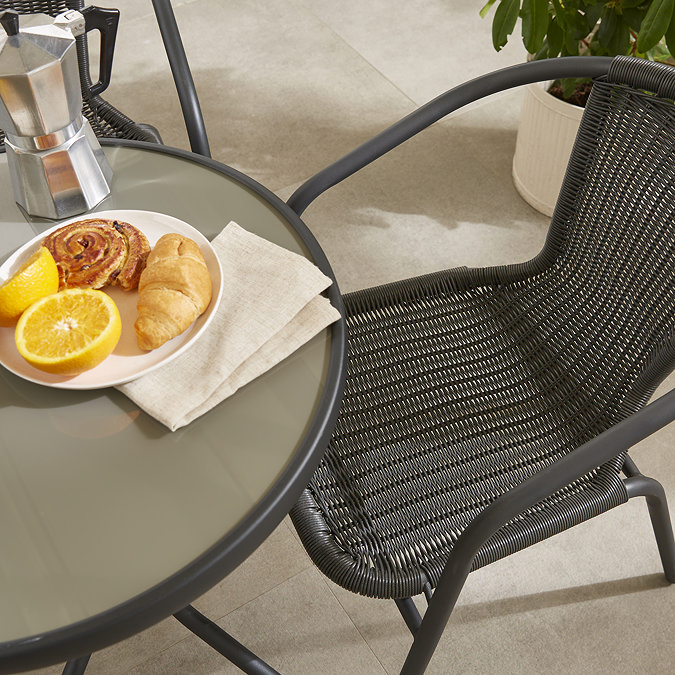 close up image of black wicker chair of bistro set, focus on material and the bowl of fruit on table at the side of the shot