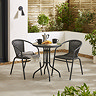 image of black steel bistro set with wicker backed chairs, on stone patio surrounded by plants