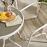 close up image on white metal bistro chair with wicker back and seat, and round table in corner topped with fruit bowl
