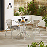image of white steel bistro set with wicker seating, on a stone patio surrounded by hedges