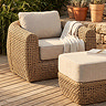 image of rounded rattan garden sofa with chunky cream cushions, on wooden decking with matching footstool