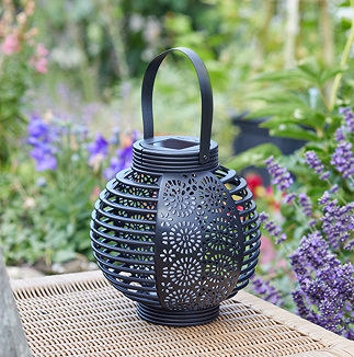 image of round ornate black lantern on wooden chair outside in front of foliage