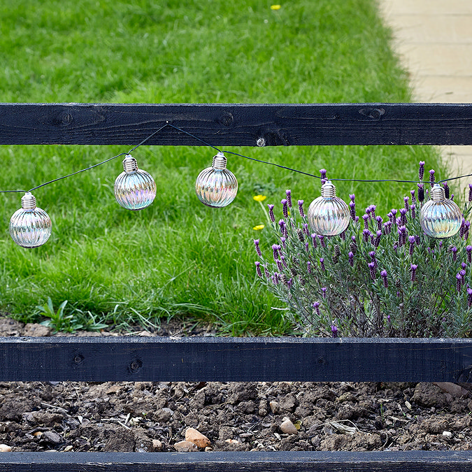 wide image of iridescent round string lights strung up on a garden fence