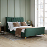 image of green velvet double bed with pleated headboard and gold feet, against sage green panelled bedroom wall