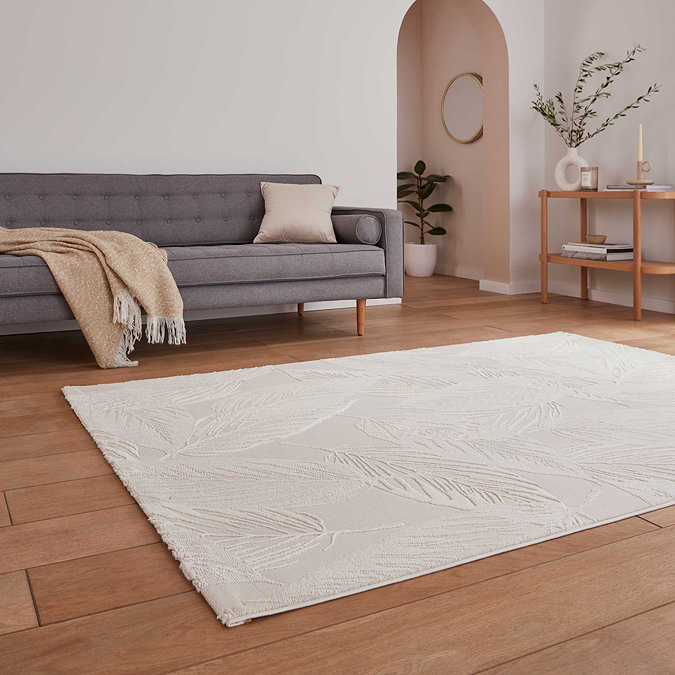 angled image of elegant cream rug with flower detailing in front of grey sofa on light wooden flooring