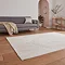 angled image of elegant cream rug with flower detailing in front of grey sofa on light wooden flooring