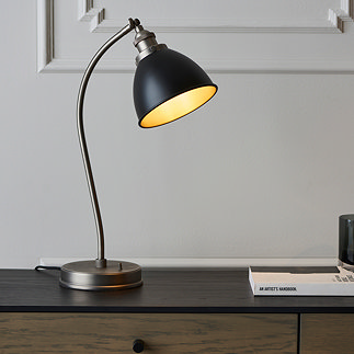 image of black metal table lamp on wooden sideboard, emitting warm glow