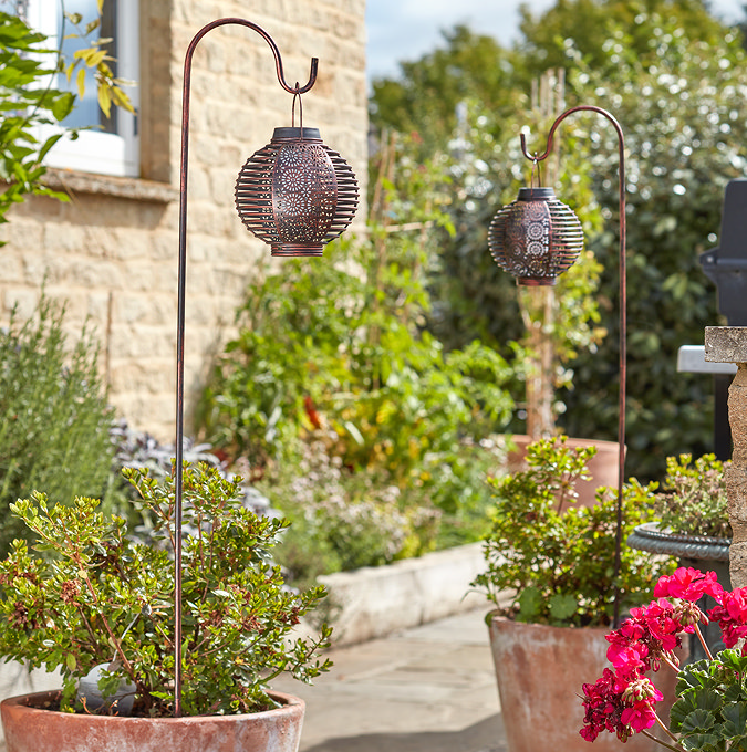 image of two tall lanterns hanging on crooks in plant pots in daylight