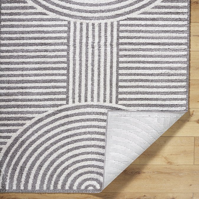 close up image of dark grey lined arch geometric rug with corner folded up to show material underneath