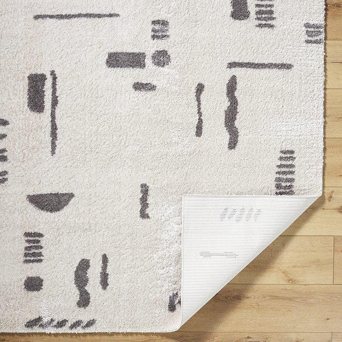 image of cream rug with dark grey abstract lines, corner folded up to reveal material underneath