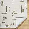 image of cream rug with green abstract line patterns, with corner folded up slightly to reveal material underneath