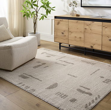image of soft cream rug with light grey abstract line patterns, corner folded up slightly to reveal material underneath