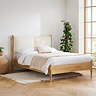 image of oak bedframe with linen headboard, against cream wall next to potted plant in bedroom