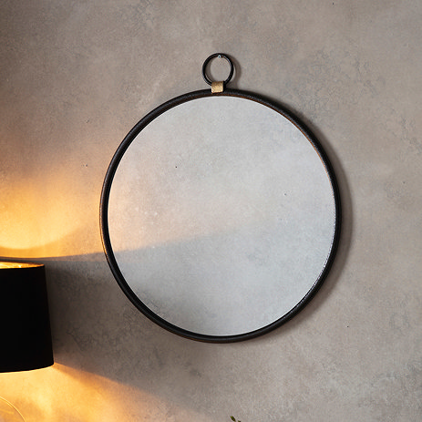 image of round black mirror on light sand coloured wall, lit up slightly by a wall light