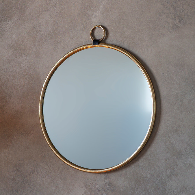 image of round gold metal mirror with a decorative loop at the top, fixed to a light grey wall