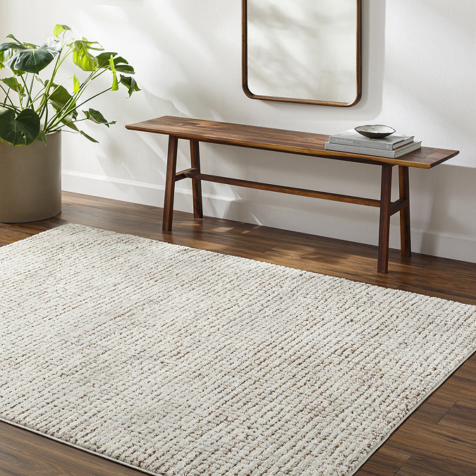 image of distressed ivory and brown rug on dark wood flooring next to walnut bench and potted plant