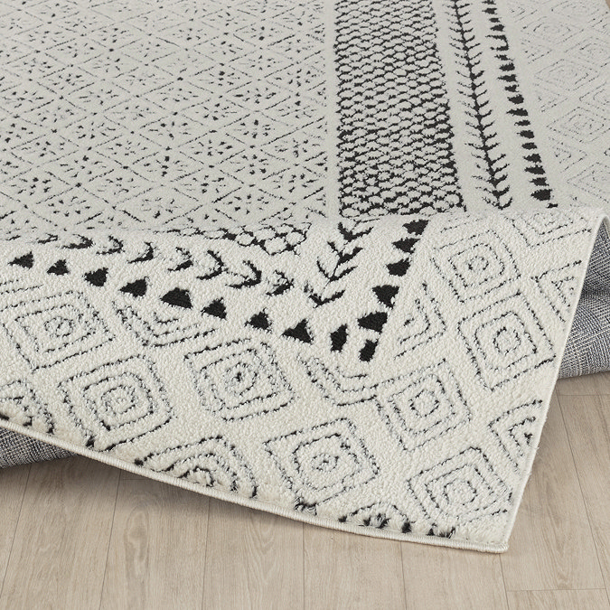 image of black and ivory diamond patterned rug on light wood flooring, lightly folded up