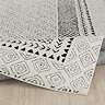 image of black and ivory diamond patterned rug on light wood flooring, lightly folded up