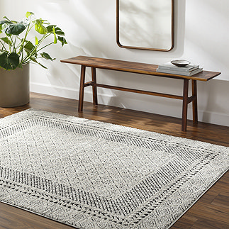 image of black and white intricate diamond patterned rug on dark wood flooring next to walnut bench and potted plant