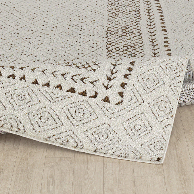 image of ivory rug with brown diamond pattern folded up slightly on light wood flooring