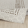 image of ivory rug with brown diamond pattern folded up slightly on light wood flooring