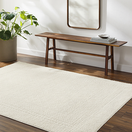 image of ivory rug with subtle diamond pattern, on dark wood flooring of apartment living area next to walnut wood bench