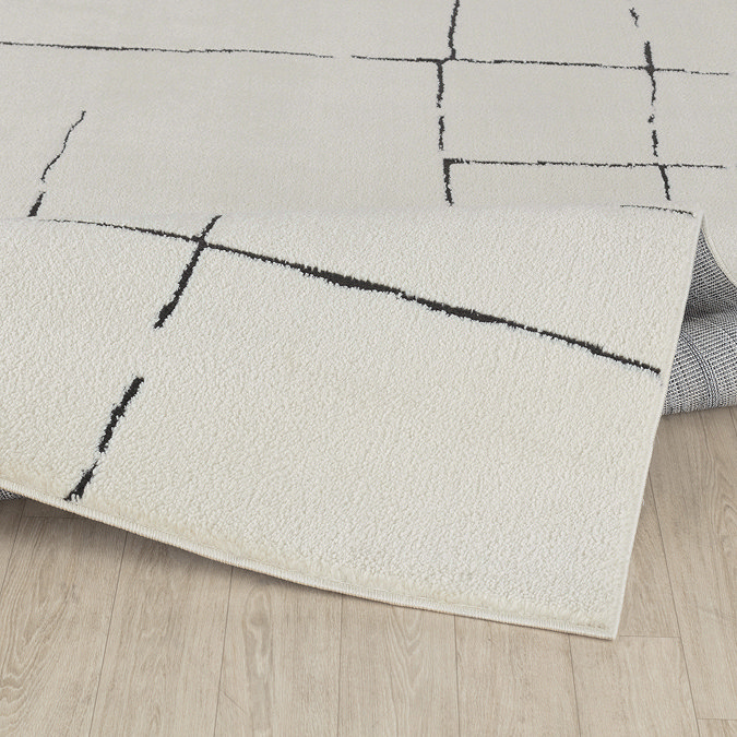 close up image of ivory rug with black line design, ruched up slightly to suggest its high pile, on light wood flooring