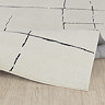 close up image of ivory rug with black line design, ruched up slightly to suggest its high pile, on light wood flooring