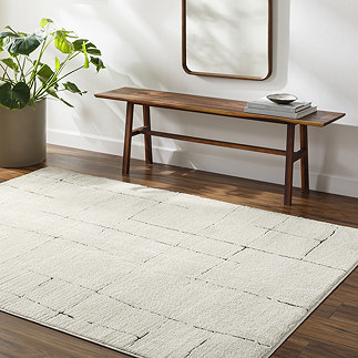 image of soft ivory rug with black scandi line design on dark wood flooring next to walnut bench and potted plant