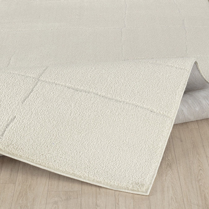 close up image of soft ivory rug ruched up slightly to show its high pile, on light wood flooring