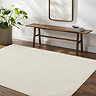image of soft ivory rug with subtle line pattern, on dark wood flooring next to walnut bench and potted plant