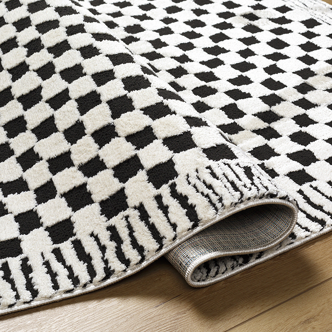 close up image of black and white checkerboard rug with abstract line border, slightly ruched up to suggest its thickness