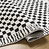 close up image of black and white checkerboard rug with abstract line border, slightly ruched up to suggest its thickness