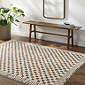 image of ivory and brown checkered rug with sleek lined border, on dark wood flooring next to walnut bench and potted plant