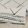 image of soft ivory rug with black diamond pattern, folded up slightly on light wood flooring