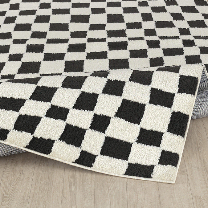 image of ivory and black checkered rug folded up slightly on light wood flooring