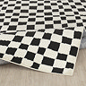 image of ivory and black checkered rug folded up slightly on light wood flooring