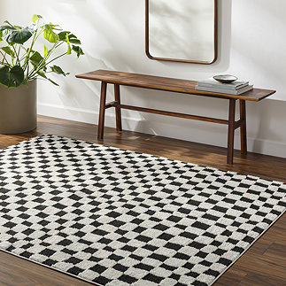 image of ivory and black checkered rug on dark wood flooring next to walnut bench and potted plant